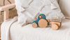 Wooden toy tractor with a small wooden trailer resting on a light fabric armchair, styled with a textured white cushion and soft neutral nursery decor.