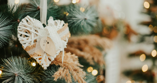 Wicker heart ornament with lace and wood details hanging on a Christmas tree with soft holiday lights—handmade, crafty look.