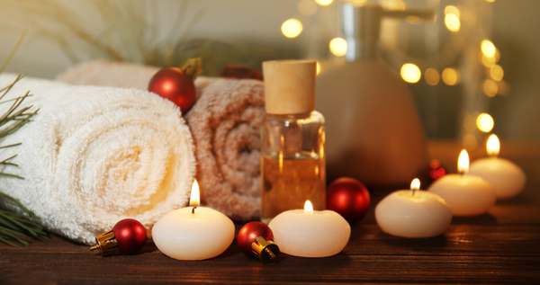Rolled towels, bath oil, and small candles with soft holiday lights—cozy spa scene.