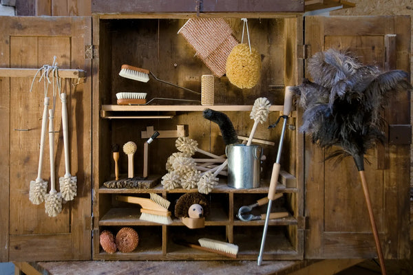  A rustic wooden cabinet filled with Redecker cleaning brushes, scrubbers, and dusters, highlighting sustainable home tools.